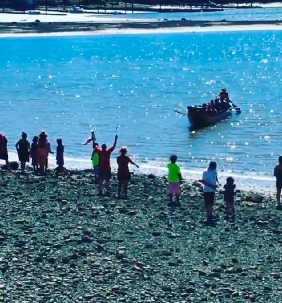 People on a shoreline welcoming an arriving canoe